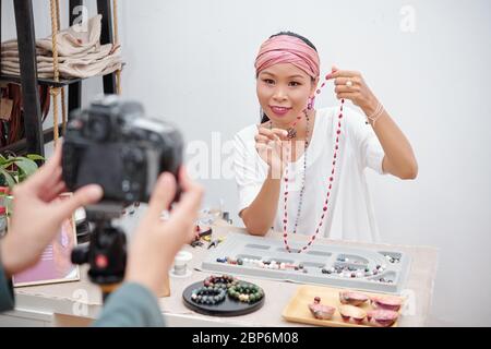 Smiling young mixed-race woman showing handmade natural stone necklace she made in workshop Stock Photo