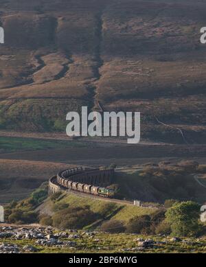 Freightliner class 66 locomotive 66510 running off Ribblehead viaduct with a merry go round coal train with the countryside towering over it