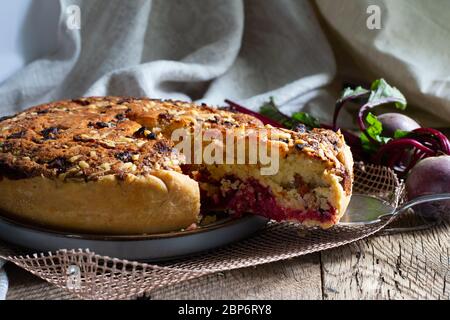 Homemade delicious beetroot pastry tart on kitchen grill with slice of cake and fresh beetroots on rustic wooden bakground. Menu, board, banner. Vintage traditional rustic kitchen. British meal Stock Photo