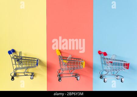 Empty supermarket shopping trolley cart on colorful yellow, red and blue background. Shopping, commerce and sale concept. Flat lay minimal composition Stock Photo