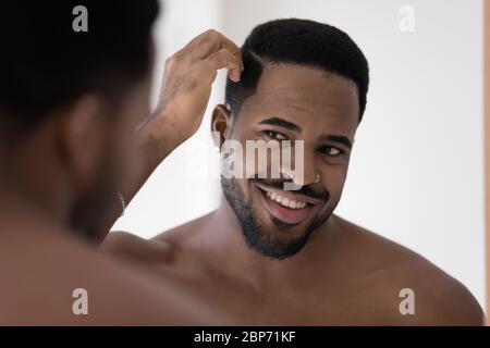Smiling african American man look in mirror in bathroom Stock Photo