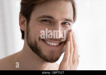 Portrait of smiling young man using facial cream Stock Photo