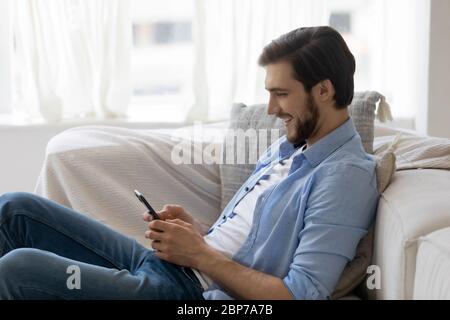 Smiling man rest on couch using smartphone gadget Stock Photo