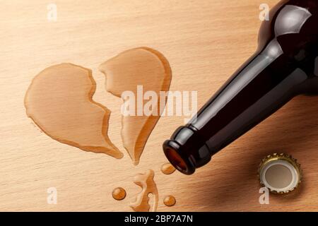 Alcoholism in the family. Broken heart, broken relationship. Beer bottle and spilled beer in the shape of a heart with a crack. Stock Photo