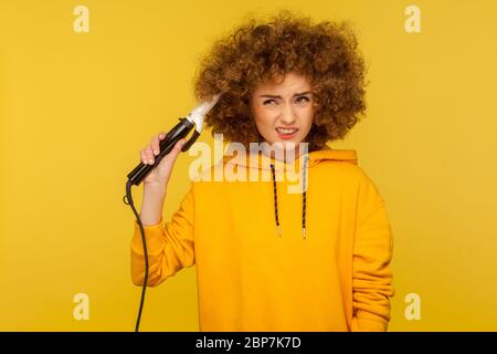 Annoyed displeased woman using curling iron to make afro hairdo, ironing hair curls and frowning dissatisfied with professional tool, bad hairstyling. Stock Photo