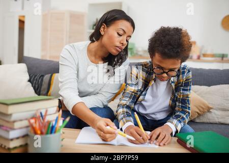 Portrait of modern African woman helping son studying at home, remote education concept