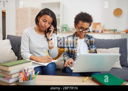 Portrait of cute African boy wearing big glasses and using laptop while studying at home with mom, copy space Stock Photo