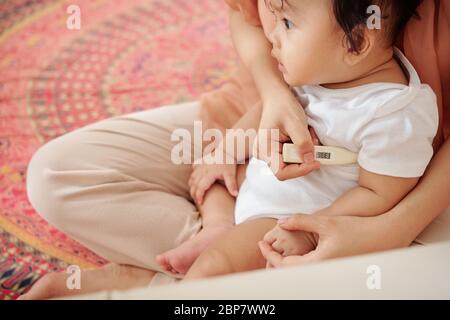 Mother checking temperature of her sick child with electric thermometer Stock Photo