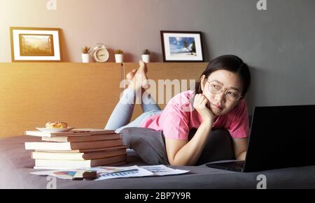 working from home, new normal concept. woman working with laptop computer on bed from her room during self isolation, feeling bored Stock Photo