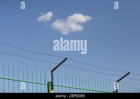 Lonely cloud in blue sky behind barbed wire Stock Photo