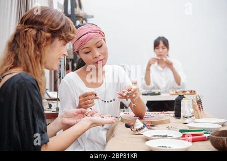 Smiling teacher looking at beautiful stone necklace her student made during lesson Stock Photo