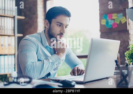 Close up portrait of tired ponder young middle eastern handsome man. He is wearing the formalwear, sitting at the workplace, looking in the laptop scr Stock Photo