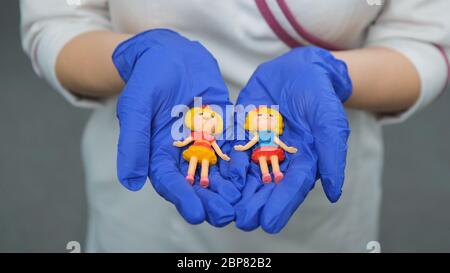 Caucasian women in white coat, violet stethoscope and rubber blue gloves holds toy figures of childrenand and raises them up to her. Front view. Close Stock Photo