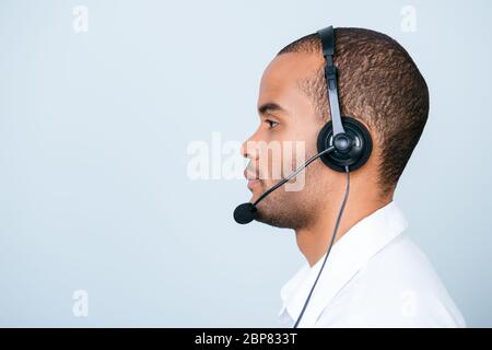 Side profile portrait of a handsome mulatto american guy call centre operator in a headset. He is isolated on a pure light background, wearing formal Stock Photo
