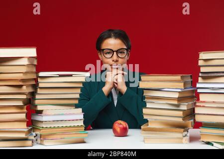 Front view portrait of young African-American woman sitting at desk between stacks of books and smiling at camera, copy space Stock Photo