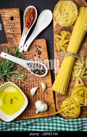 Ingredients for Italian cooking, pasta, herb, spices and olive oil on black stone table, top view. Stock Photo