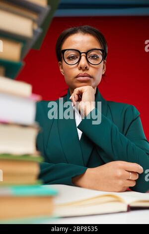 Low angle view at strict female teacher looking at camera with stack of books in foreground, shot on red Stock Photo