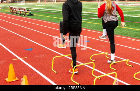 Rear angled view of two high school sprinter runners in a sprint techique A-Position over yellow mini hurdles on a red track. Stock Photo