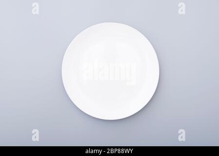 White ceramic plate on gray table, top view of white dish. Round plate, bowl. Stock Photo
