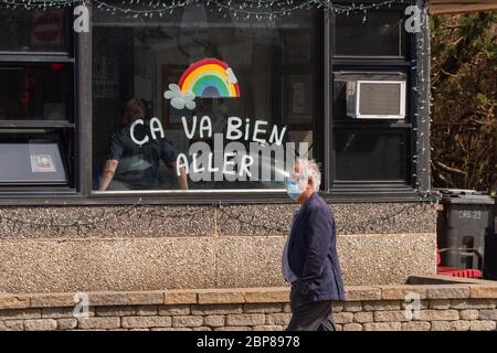 Montreal, CA - 17 May 2020: Man with face mask for protection from COVID-19 walking in front of rainbow drawing on Masson street. Stock Photo