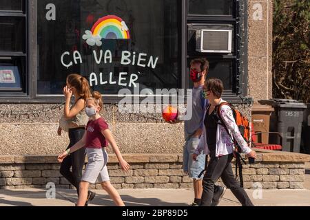 Montreal, CA - 17 May 2020: Family with face masks for protection from COVID-19 walking in front of rainbow drawing on Masson street. Stock Photo