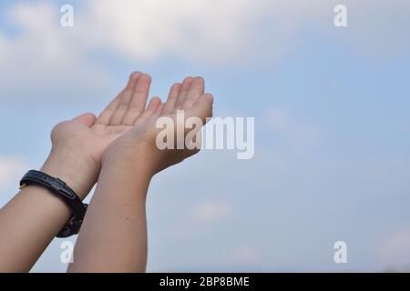 Children's open hands praying for blessing from god over blue sky background. Stock Photo