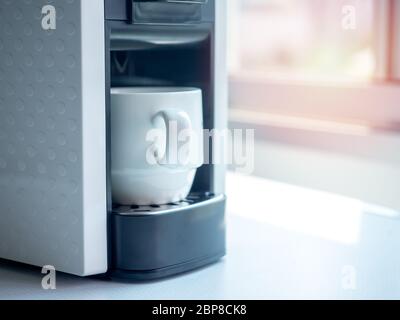 White ceramic coffee cup on coffee machine on white table near the window with sunlight in the morning with copy space. Stock Photo