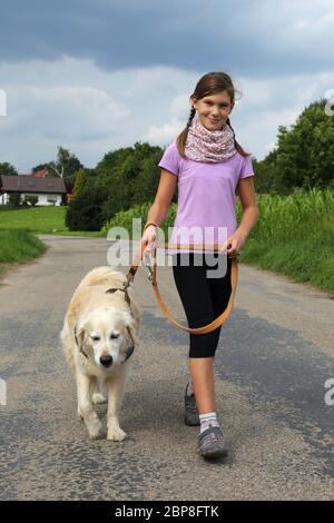 Ein Mädchen geht draußen mit einem Hund spazieren auf einem Weg Stock Photo