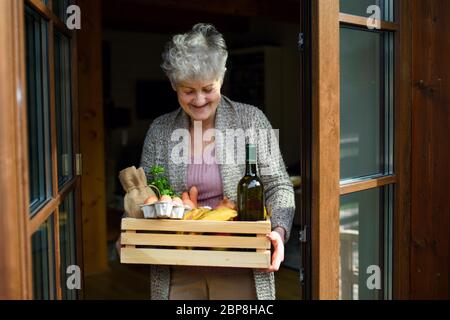 Front view of woman holding food shopping delivery by front door. Stock Photo