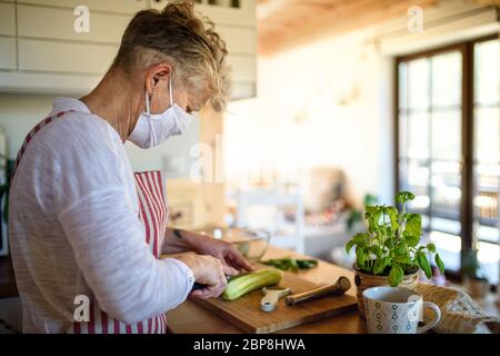 Woman with face mask cooking indoors at home, corona virus concept. Stock Photo