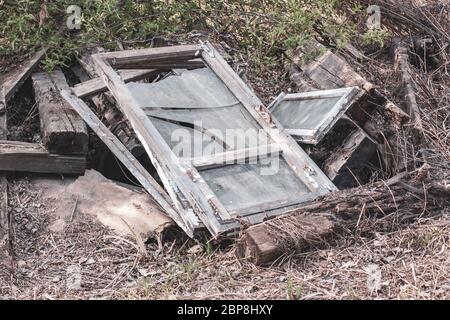 Old window frames with broken glass and thick wooden beams lie on the ground. Glasses are dirty. Around the withered grass. Horizontal. Stock Photo