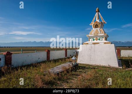 A Buddhist stupa stands in a field against a blue sky. White Tibetan stupa with decorations. Mountain on the horizon. Horizontal. Stock Photo