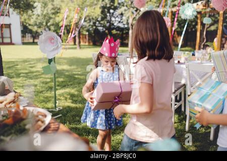 Small girls outdoors in garden in summer, holding presents. Stock Photo