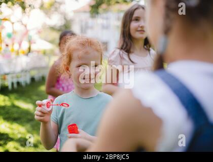 Small children outdoors in garden in summer, playing with bubbles. Stock Photo