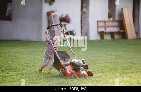 Down syndrome child with lawn mower walking outdoors in garden. Stock Photo