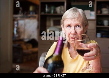 Older adult female offering a bottle of wine and glass sitting alone Stock Photo
