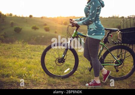 Young woman having fun near countryside park, riding bike, traveling at spring day. Calm nature, spring day, positive emotions. Sportive, active leisure activity. Walking in motion, blossoming nature. Stock Photo
