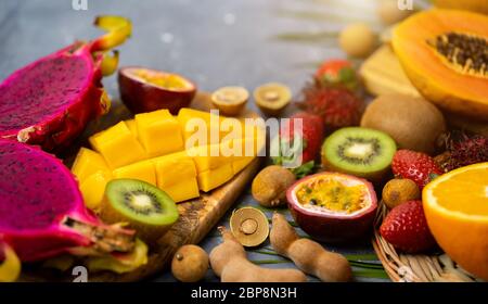 Set of exotic thai fruits over gray blue background. Fresh sliced papaya, kiwi, passion fruit, longan,strawberry on wooden cutting boards . Copy space Stock Photo