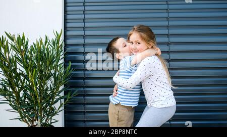 Small girl and boy standing outdoors at home, hugging. Stock Photo