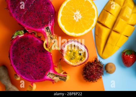Closeup shot of halves fresh ripe exotic tropical fruits. Dragon fruit, orange, passion fruit, rambutan on orange background. Top view, flat lay. Summ Stock Photo
