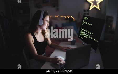 Young girl with headphones and computer sitting indoors, playing games concept. Stock Photo