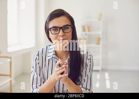 Hispanic teacher with glasses looking at the camera smiling. A college university teacher teaches remotely using a video call application gadget. Stock Photo