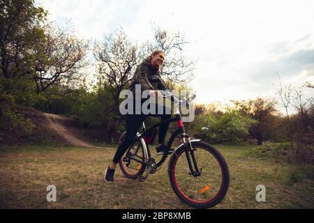 Young man having fun near countryside park, riding bike, traveling at spring day. Calm nature, spring day, positive emotions. Sportive, active leisure activity. Walking in motion, blossoming nature. Stock Photo