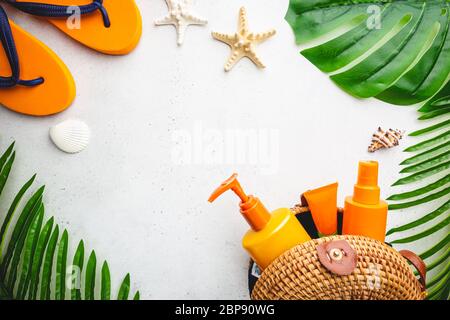 Sunscreen bottles arranged in straw bag on white background with palm leaves, top view Stock Photo