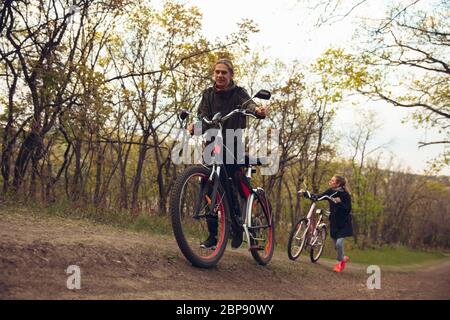 Best friends having fun near countryside park, riding bikes, spending time healthy. Calm nature, spring day, positive emotions. Sportive, active leisure activity. Traveling or walking together. Stock Photo