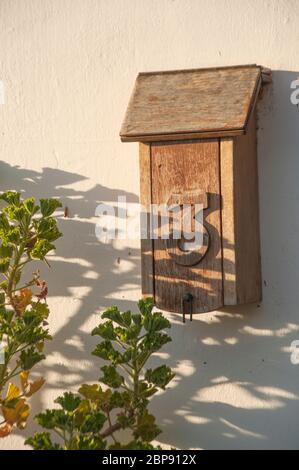 Old wooden postbox #3 mounted on a wall, in shadows of plants. Number 3 is carved on the door. Sadows give it an air of mystery Stock Photo