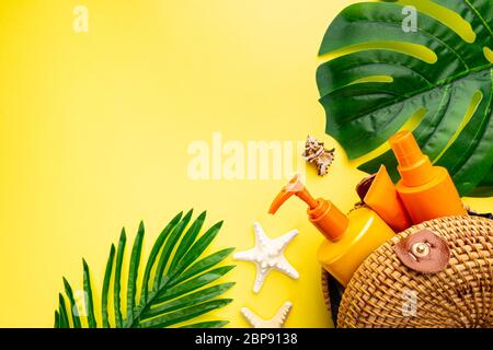 Sunscreen bottles arranged in straw bag on a bright yellow background with palm leaves, top view Stock Photo