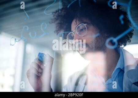 Doctor making notes in hospital, corona virus concept. Shot through glass. Stock Photo