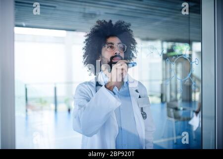 Doctor making notes in hospital, corona virus concept. Shot through glass. Stock Photo
