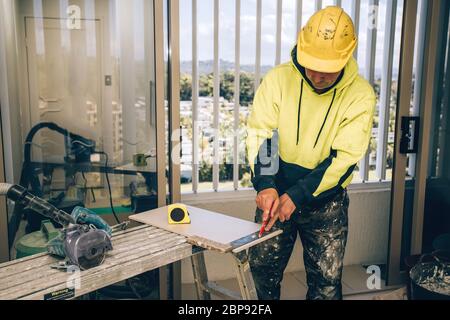 Man marking marks with pencil on a tile to be cut. Laying ceramic floor tiles, home renovation. Stock Photo